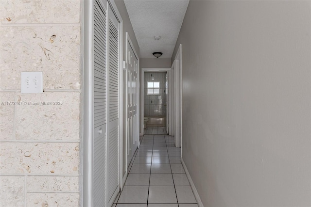 corridor with light tile patterned floors, baseboards, and a textured ceiling