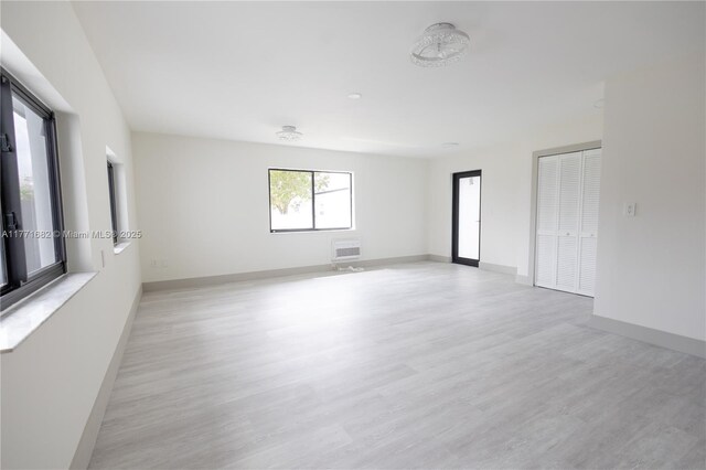 empty room with heating unit, baseboards, and light wood-type flooring