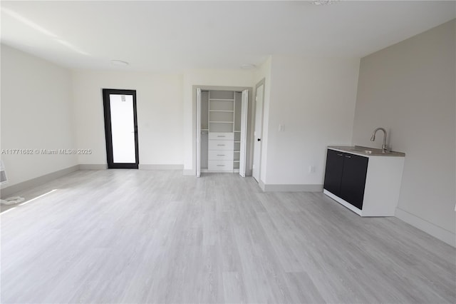 unfurnished living room featuring baseboards, light wood-type flooring, and a sink