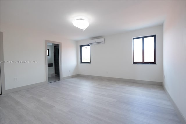 unfurnished room with a wall unit AC, light wood-style floors, and baseboards