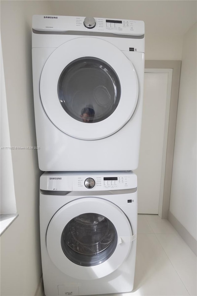 washroom featuring light tile patterned flooring, stacked washer / dryer, and laundry area