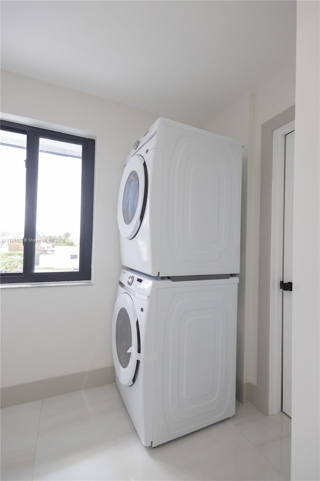 clothes washing area featuring stacked washing maching and dryer, laundry area, and light tile patterned floors