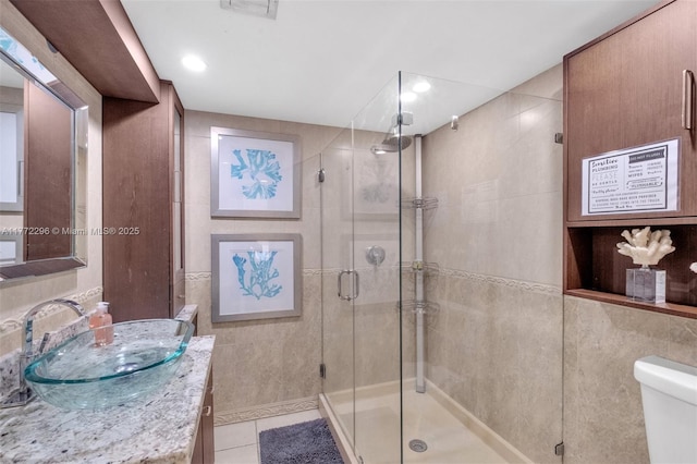 full bath featuring tile patterned floors, a stall shower, vanity, tile walls, and toilet