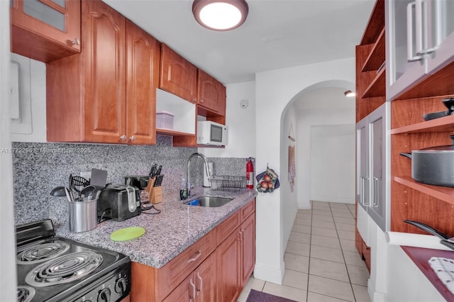 kitchen with light tile patterned floors, arched walkways, a sink, white microwave, and black electric range oven
