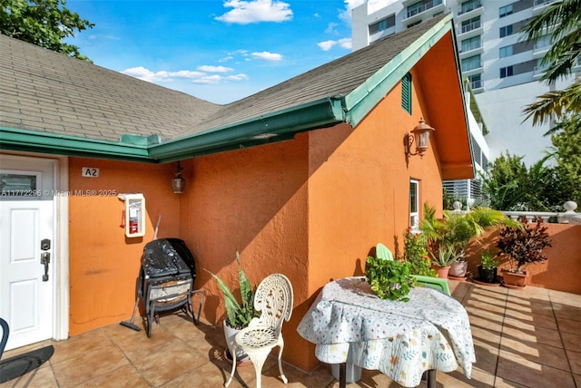 exterior space featuring a patio area, a shingled roof, and stucco siding