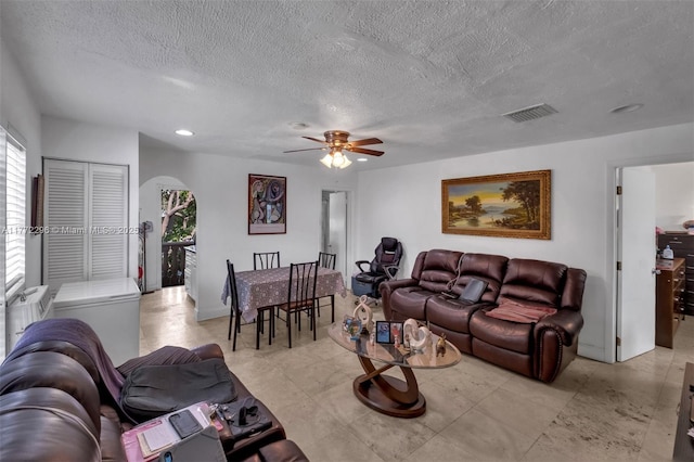 living area featuring a ceiling fan, visible vents, arched walkways, and a textured ceiling