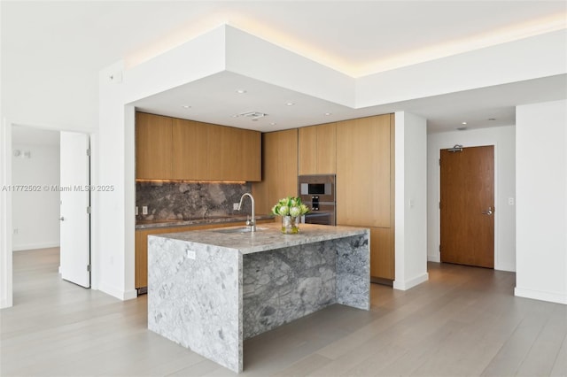 kitchen featuring oven, modern cabinets, light wood finished floors, backsplash, and light stone countertops