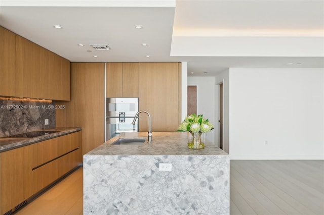 kitchen with light stone counters, a sink, modern cabinets, light wood-style flooring, and visible vents