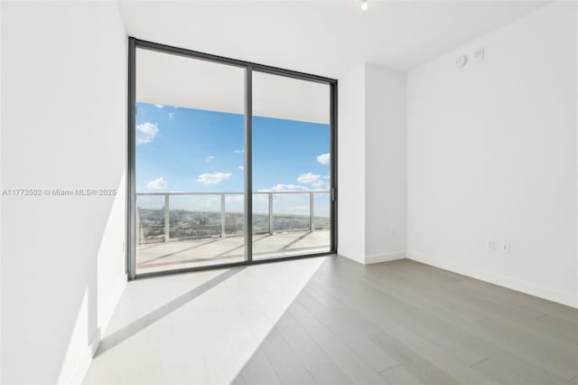 spare room with baseboards, a wall of windows, and wood finished floors