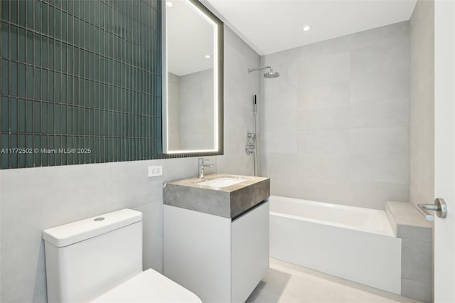 bathroom featuring toilet, shower / bathtub combination, vanity, and tile walls