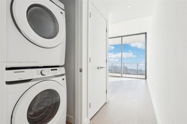 clothes washing area featuring stacked washer / drying machine, light wood-type flooring, baseboards, and laundry area