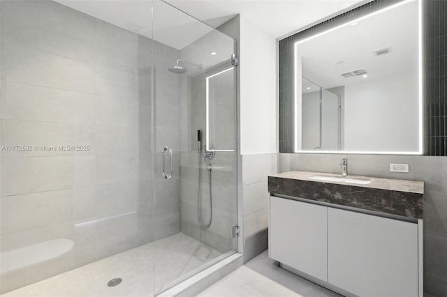 full bath featuring a shower stall, vanity, visible vents, and tile walls
