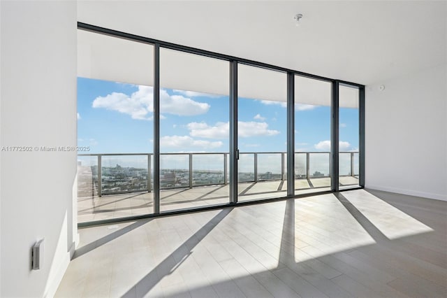 spare room featuring baseboards, wood finished floors, floor to ceiling windows, and a healthy amount of sunlight