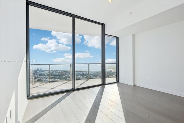 unfurnished room with baseboards, wood finished floors, and floor to ceiling windows