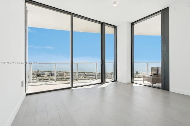 unfurnished room with baseboards, wood finished floors, and a wall of windows