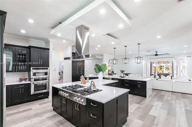 kitchen featuring a large island, open floor plan, island range hood, dark cabinets, and light countertops
