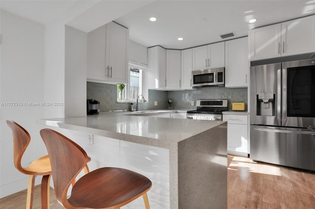 kitchen with a peninsula, visible vents, light stone counters, a sink, and stainless steel appliances