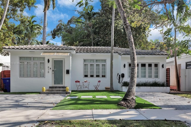 view of front facade featuring entry steps, stucco siding, a tile roof, and a front yard