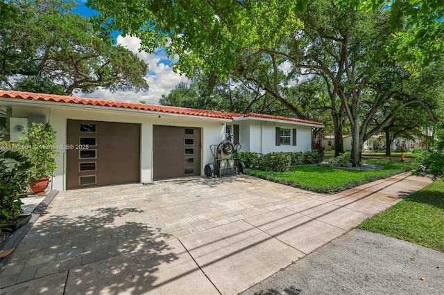 view of front facade featuring a tile roof, stucco siding, an attached garage, decorative driveway, and a front yard