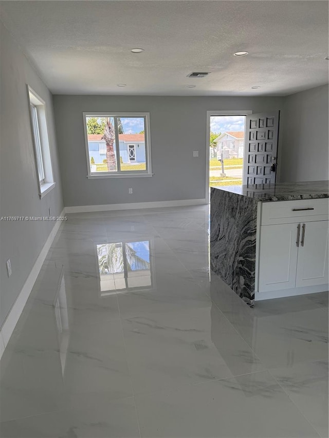 spare room with marble finish floor, visible vents, a textured ceiling, and a wealth of natural light