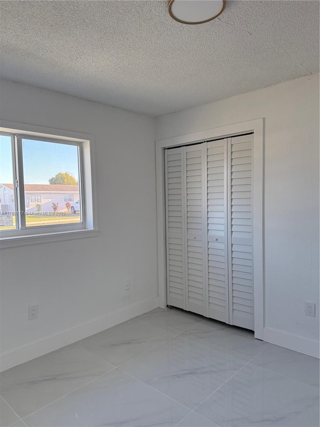 unfurnished bedroom featuring baseboards, a textured ceiling, and a closet