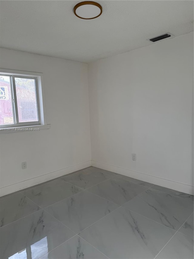 spare room with marble finish floor, baseboards, and visible vents