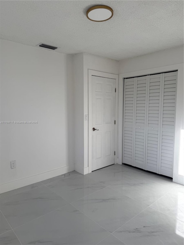 unfurnished bedroom featuring a closet, a textured ceiling, visible vents, baseboards, and marble finish floor