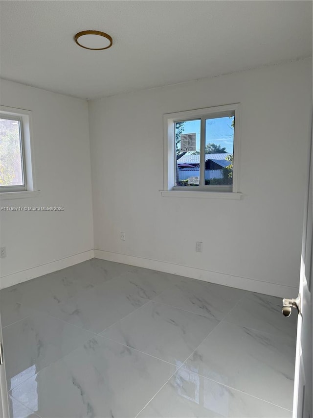 unfurnished room featuring marble finish floor and baseboards