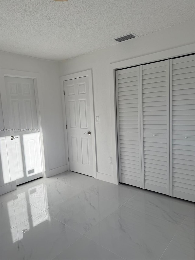 unfurnished bedroom featuring a closet, a textured ceiling, visible vents, baseboards, and marble finish floor