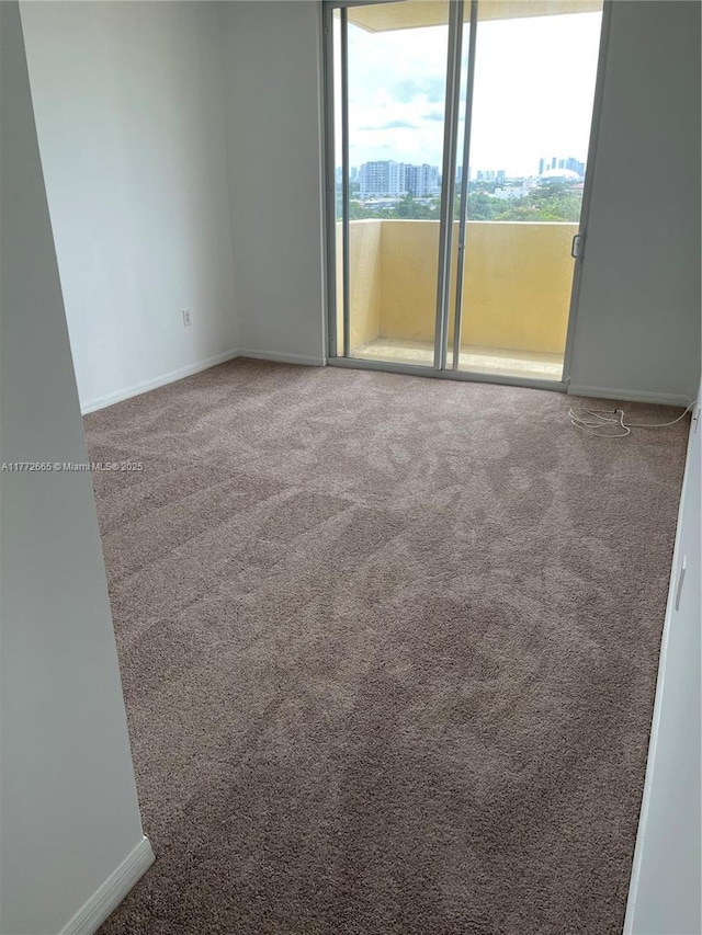 empty room featuring baseboards, a city view, and carpet