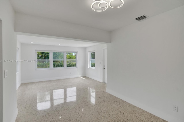 empty room with baseboards, visible vents, and speckled floor