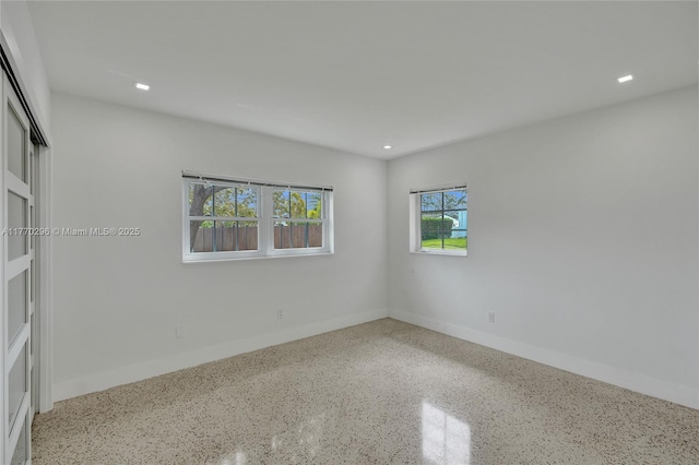 empty room featuring baseboards, speckled floor, and recessed lighting