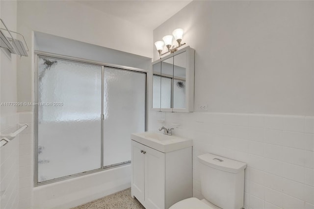 bathroom with toilet, speckled floor, vanity, bath / shower combo with glass door, and tile walls