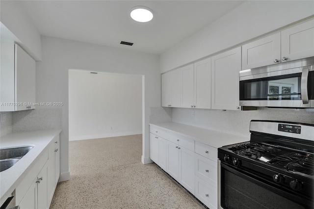 kitchen with stainless steel microwave, range with gas stovetop, light countertops, and white cabinetry