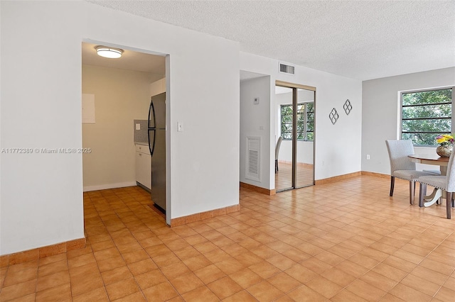 empty room with a textured ceiling, a healthy amount of sunlight, baseboards, and visible vents
