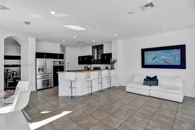 721 Ranch Rd, Weston, FL 33326 - kitchen featuring stainless steel appliances, a peninsula, dark cabinetry, a kitchen bar, and arched walkways