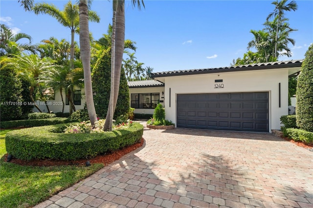 mediterranean / spanish home featuring a tiled roof, a garage, stucco siding, and decorative driveway