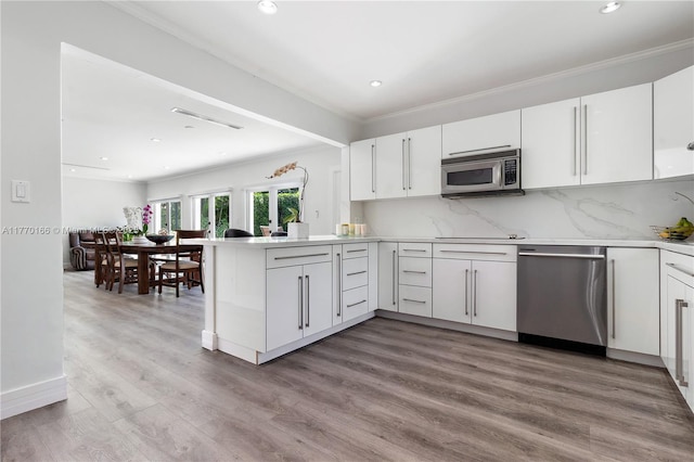 kitchen featuring a peninsula, ornamental molding, white cabinets, wood finished floors, and stainless steel appliances