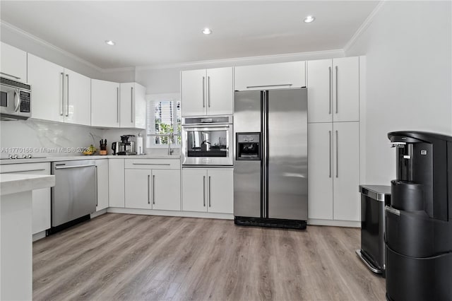 kitchen featuring white cabinets, ornamental molding, light countertops, appliances with stainless steel finishes, and light wood finished floors
