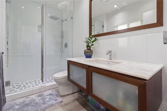 bathroom featuring a shower stall, wood finished floors, vanity, and toilet