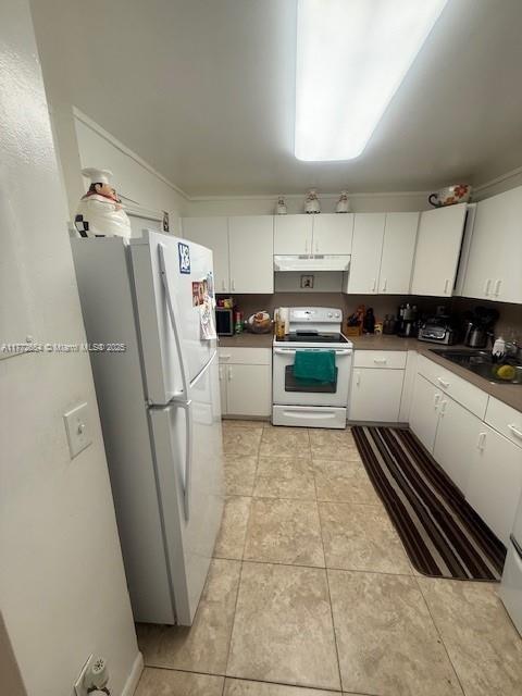 kitchen with a sink, under cabinet range hood, light tile patterned floors, white appliances, and white cabinets