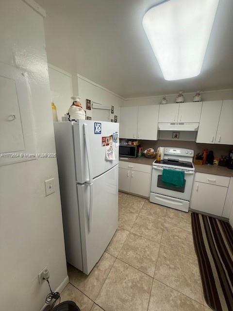 kitchen featuring light tile patterned flooring, under cabinet range hood, white cabinetry, and white appliances