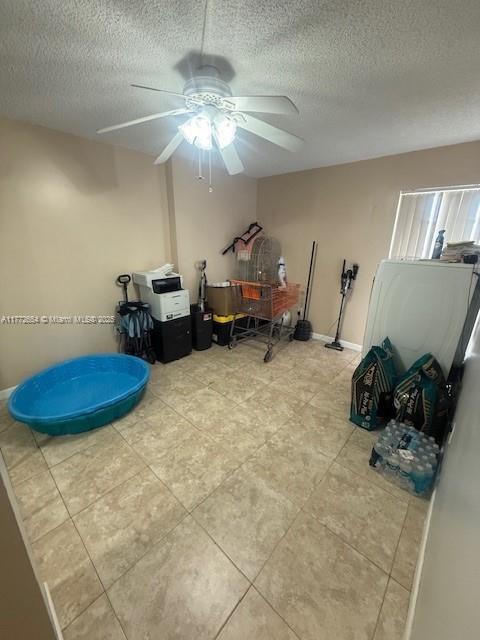 misc room with a textured ceiling, ceiling fan, baseboards, and light tile patterned floors