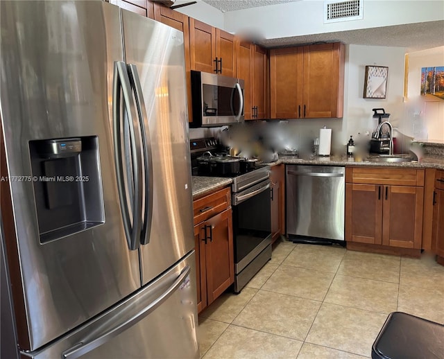 kitchen featuring light tile patterned floors, visible vents, appliances with stainless steel finishes, a sink, and brown cabinets