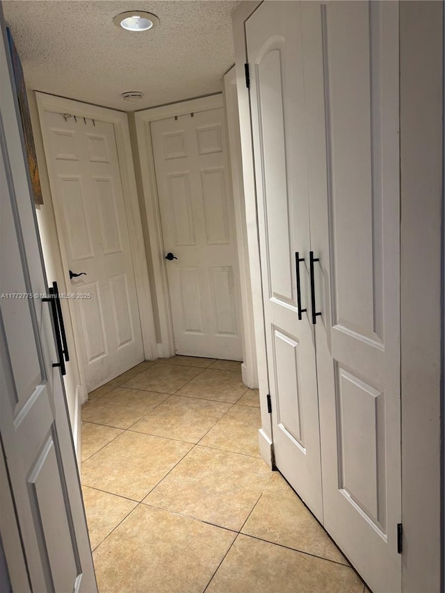 hall with a textured ceiling and light tile patterned flooring