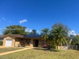ranch-style home with roof mounted solar panels, driveway, a front yard, and an attached garage