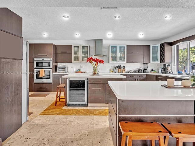 9461 SW 128th St, Miami, FL 33176 - kitchen with light countertops, wall chimney exhaust hood, dark brown cabinets, beverage cooler, and a kitchen breakfast bar