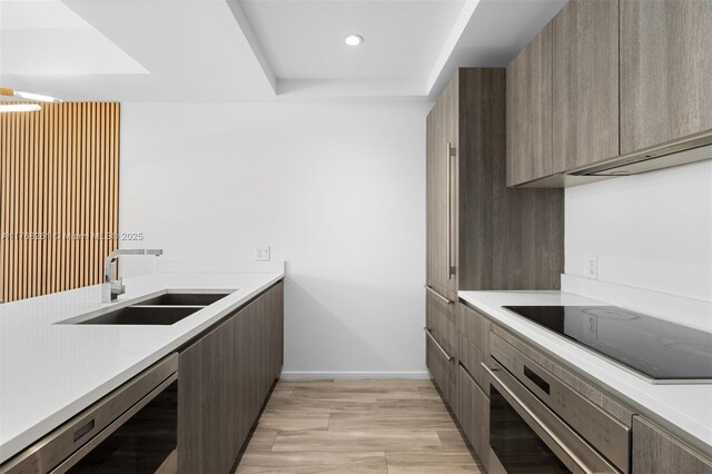 kitchen featuring light countertops, stainless steel oven, a sink, modern cabinets, and black electric cooktop