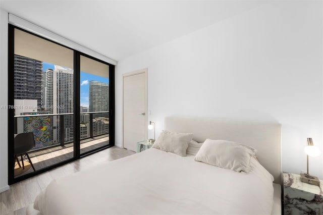 bedroom with a city view, expansive windows, access to exterior, and wood finished floors