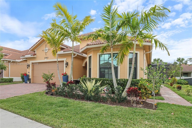 mediterranean / spanish house with a garage, a front yard, stucco siding, and decorative driveway